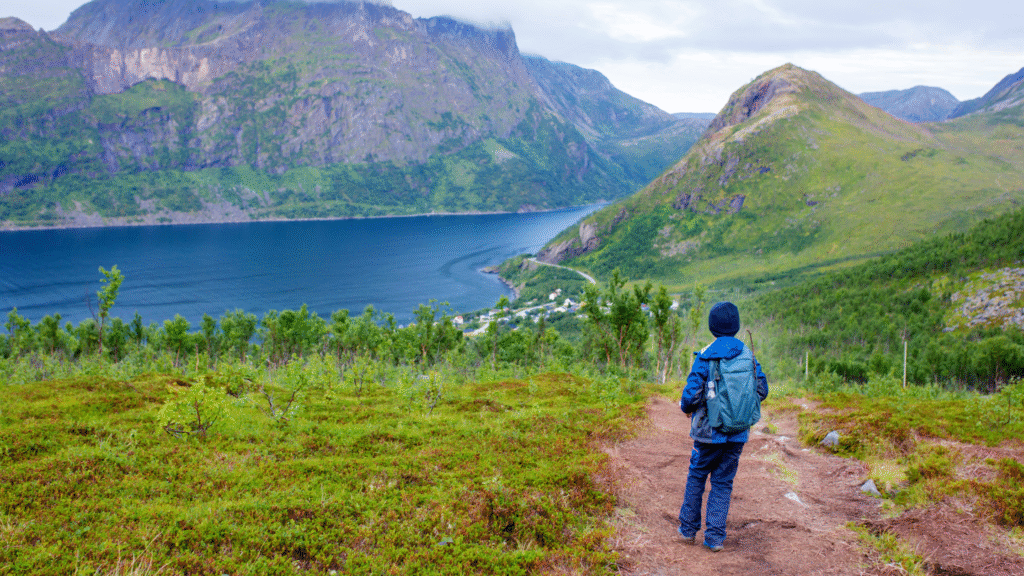 Traveler hiking along a Scandinavian fjord trail surrounded by mountains and clear water, symbolizing sustainable travel in 2025.