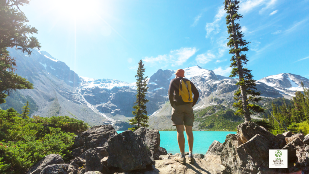 Man hiking on a mountain trail overlooking a beautiful lake and rugged peaks in Canada