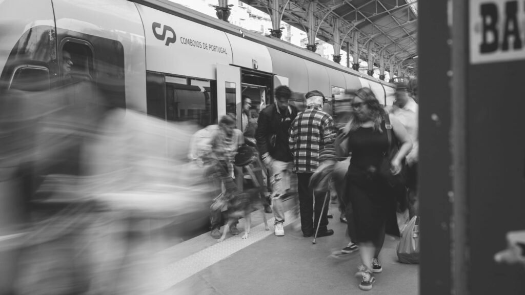 A black and white scene of commuters at a Lisbon train station, showcasing urban movement.